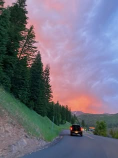 a car driving down the road at dusk with pink clouds in the sky above it