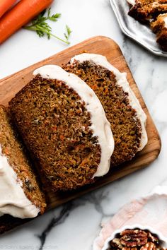 carrot cake with cream cheese frosting on a cutting board next to sliced carrots