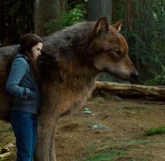 a woman standing next to a wolf in the woods