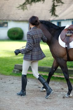 a woman in riding gear walking a horse