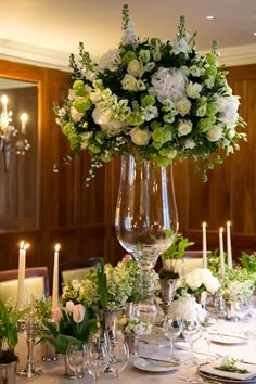 a tall vase filled with white flowers sitting on top of a table next to candles