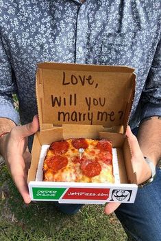 a man holding up a box with pizza in it that says love, will you marry me?