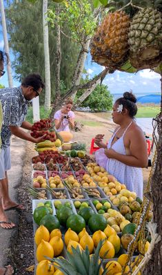 people standing around a fruit stand with pineapples, melons and other fruits