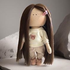 a doll with long brown hair wearing a white shirt and striped pants sitting on a bed