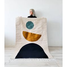 a woman holding up a large blanket with circles and dots on it in front of a white wall