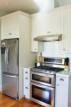 a stainless steel refrigerator and stove in a white kitchen with wood floors, cabinets and drawers