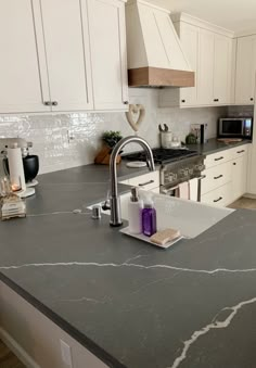 a kitchen with white cabinets and grey counter tops, along with an island in the middle