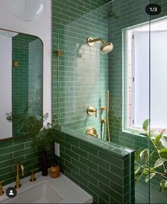 a green tiled bathroom with gold fixtures and plants in the window sill next to the sink