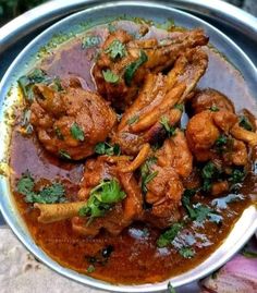 a metal bowl filled with meat covered in gravy and garnished with cilantro