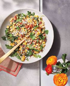 a white plate topped with salad next to orange flowers and a wooden spoon on top of a table