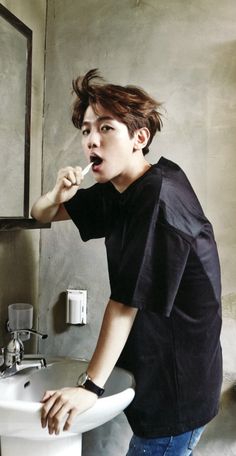 a young man brushing his teeth in front of a bathroom sink with a mirror above it