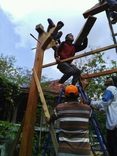 three men working on a wooden structure with ladders in the foreground and trees in the background