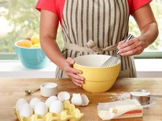 a woman in an apron holding a yellow bowl on top of a wooden table next to utensils