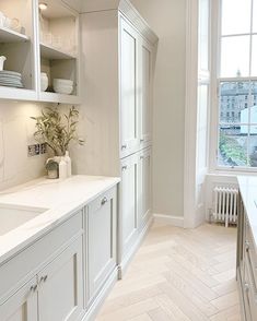 a kitchen with white cabinets and wood flooring next to a large window in the corner