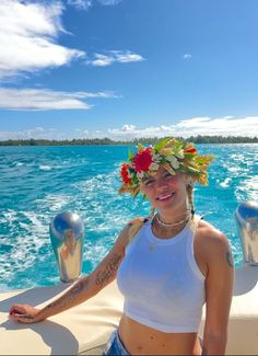 a woman with flowers in her hair standing on the back of a boat looking at the camera