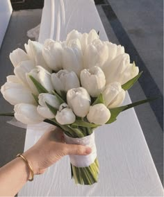 a bouquet of white tulips being held by a woman's hand on a table