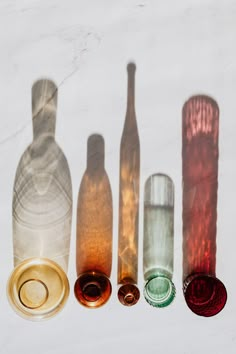 four different colored glass bottles sitting next to each other on a white surface with shadows