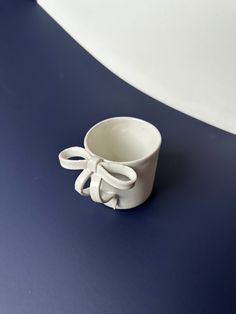 a small white cup with a bow on the side sitting on a blue table top