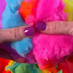 a woman's hand with purple nail polish holding colorful cotton balls