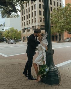 a bride and groom kissing under a street light on a city sidewalk in front of tall buildings