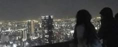 three people standing on top of a tall building at night with city lights in the background