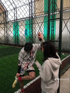 a woman holding a soccer ball up to her face while standing next to a fence