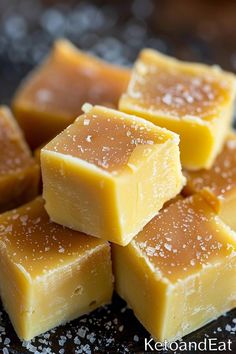 several pieces of caramel fudge sitting on top of a black plate covered in sugar