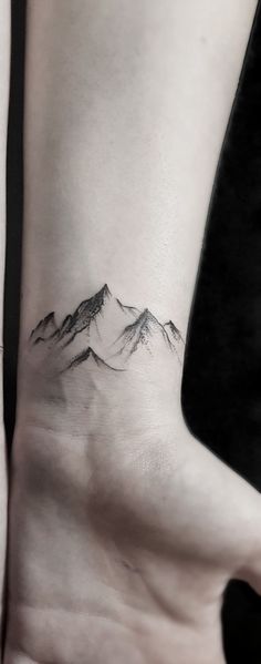 a small mountain tattoo on the left side of the arm, with snow capped mountains in the background