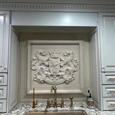 a kitchen with marble counter tops and white cabinets, along with an ornate coat of arms on the wall