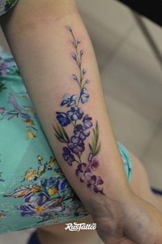 a woman's arm with purple flowers and leaves on the left side of her arm