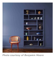 a chair sitting in front of a blue book shelf filled with vases and bowls