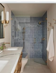 a bathroom with blue tile and gold fixtures on the shower wall, along with two sinks