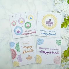 three happy diwali greeting cards sitting on top of a table next to flowers