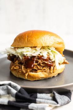 a pulled pork sandwich with cole slaw on a black plate next to a blue and white dish towel