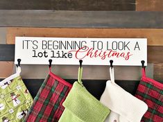 christmas stockings hanging from hooks on a wooden wall with a sign saying it's beginning to look a lot like christmas