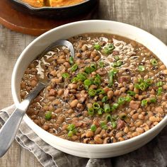 a white bowl filled with beans and green onions on top of a wooden table next to a casserole dish