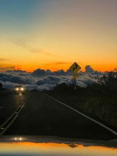 the sun is setting over some clouds in the sky and cars are driving down the road