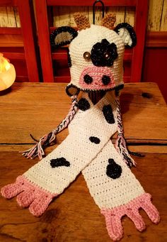 a crocheted cow scarf sitting on top of a wooden table next to a lit candle