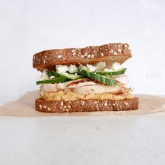 a sandwich with chicken, cucumber and lettuce on it sitting on a piece of parchment paper