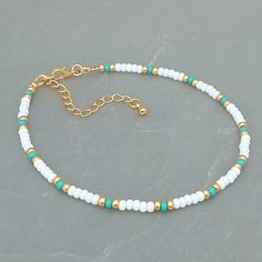 a white and green beaded bracelet with gold accents on a gray surface, the beads are