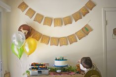 a little boy sitting at a table in front of a cake and balloons with the words adventure awaits on it