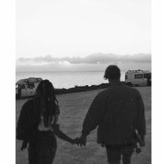 a man and woman holding hands in front of the ocean with an rv parked on the shore