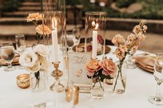 a table topped with vases filled with flowers next to candles and place card holders