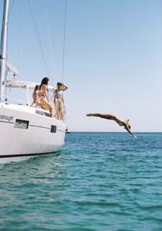 two people on a sailboat in the ocean with a bird flying over them and another person diving into the water