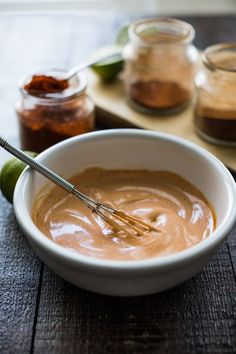 a white bowl filled with peanut butter on top of a wooden table next to jars