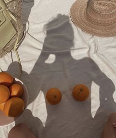 two bowls of oranges are sitting on a table with straw hats and a handbag