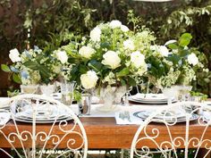 the table is set with white flowers and place settings for two people to sit at