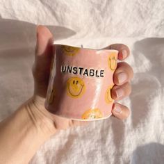 a hand holding a pink coffee mug with smiley faces on it that says unstable