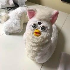 a white stuffed animal with big eyes and a yellow beak sitting on top of a table