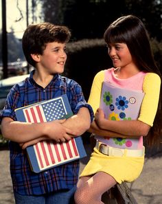 a boy and girl standing next to each other with an american flag on their lap